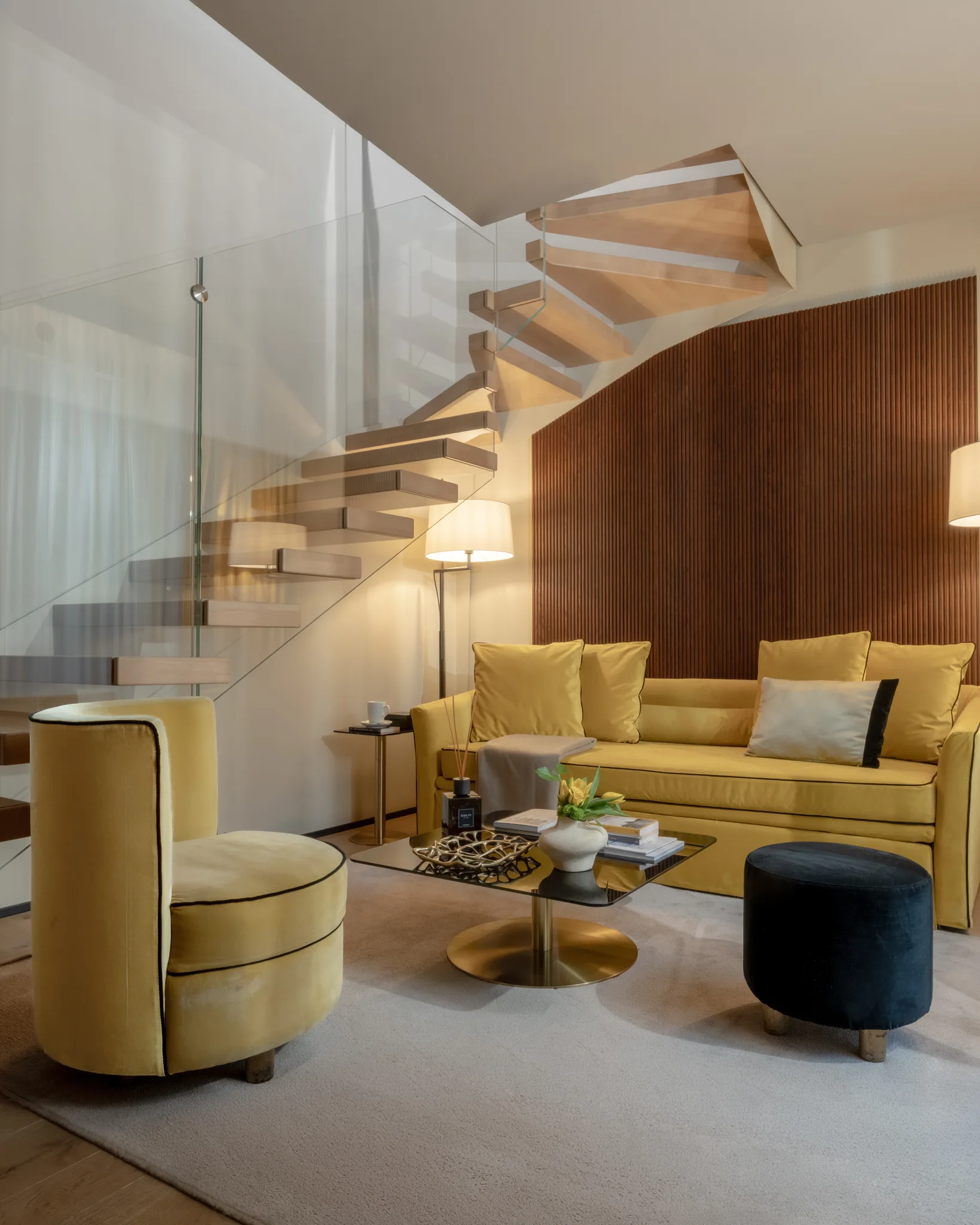 Suite Duplex — glass staircase, walnut panelling, velvet sofa, afternoon light